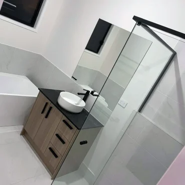 Sparkling clean contemporary bathroom after professional cleaning service. Features include a minimalist wood vanity, matte black fixtures, and pristine white marble tiling with a frameless glass shower.